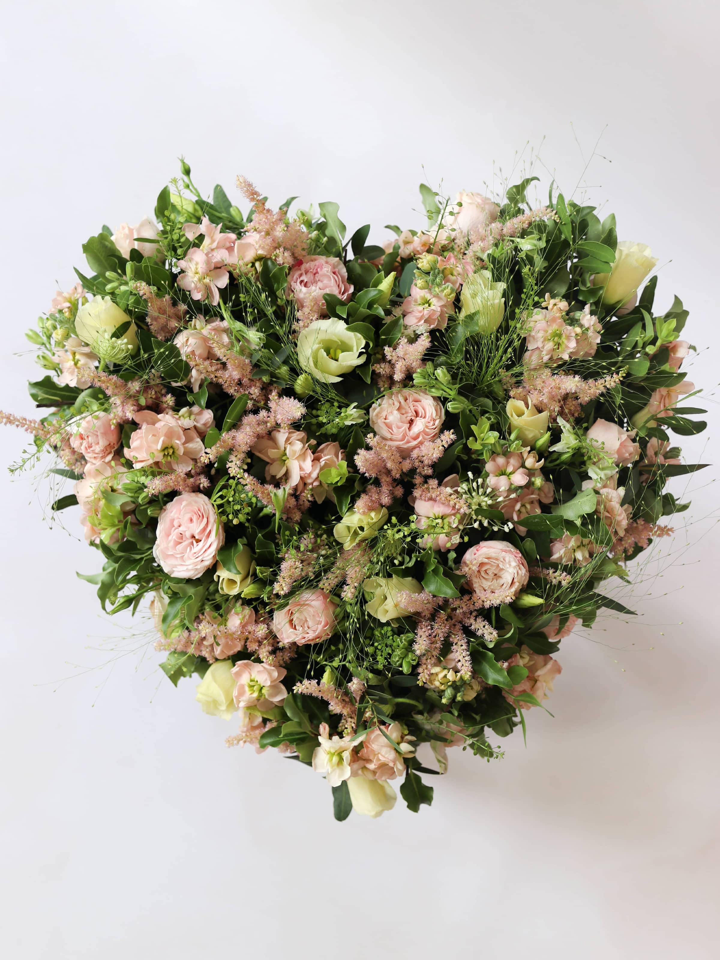 Heart shaped funeral posy with pink and green colours on a white background sitting on a wooden stool