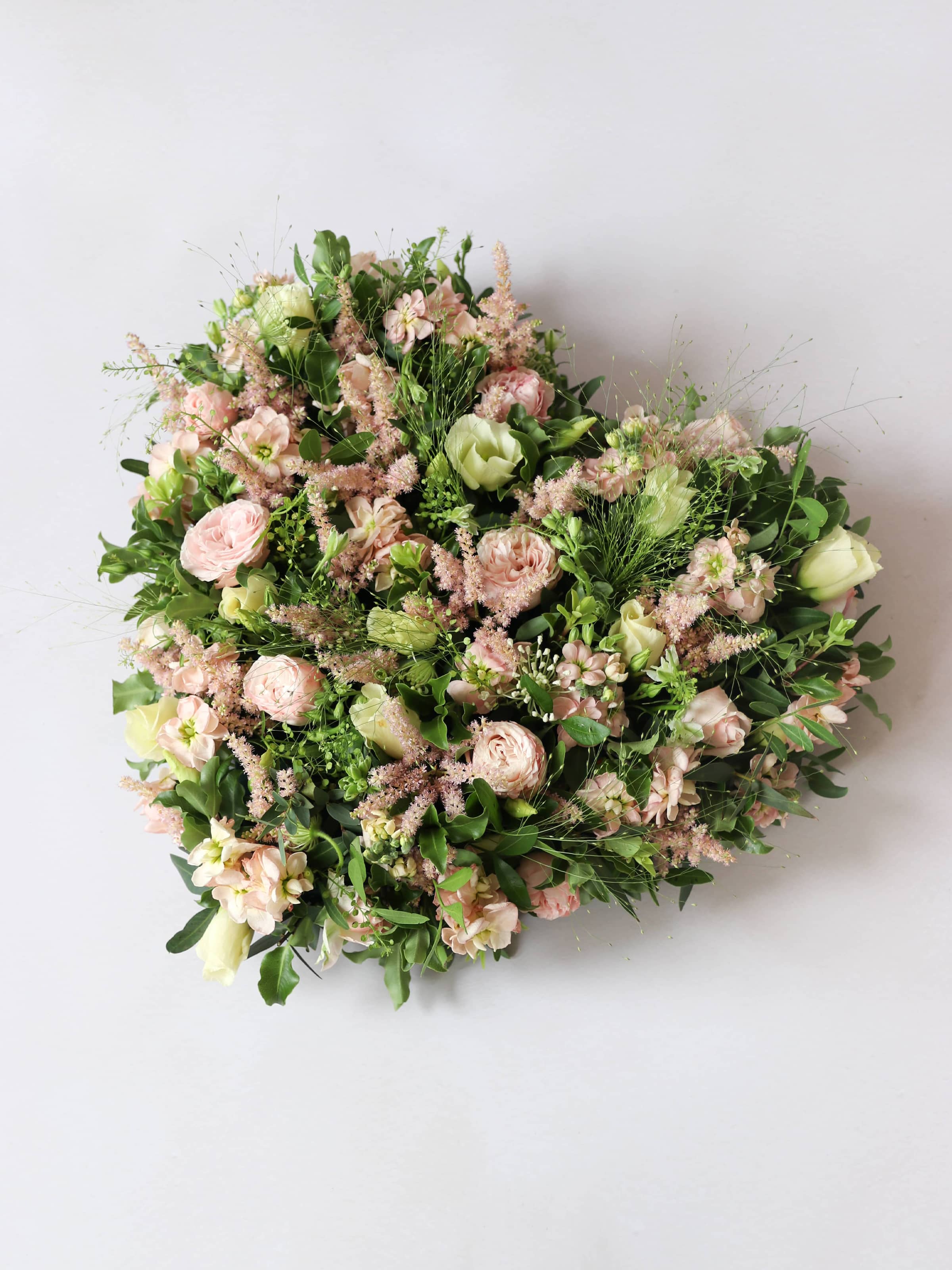 Heart shaped funeral posy with pink and green colours on a white background