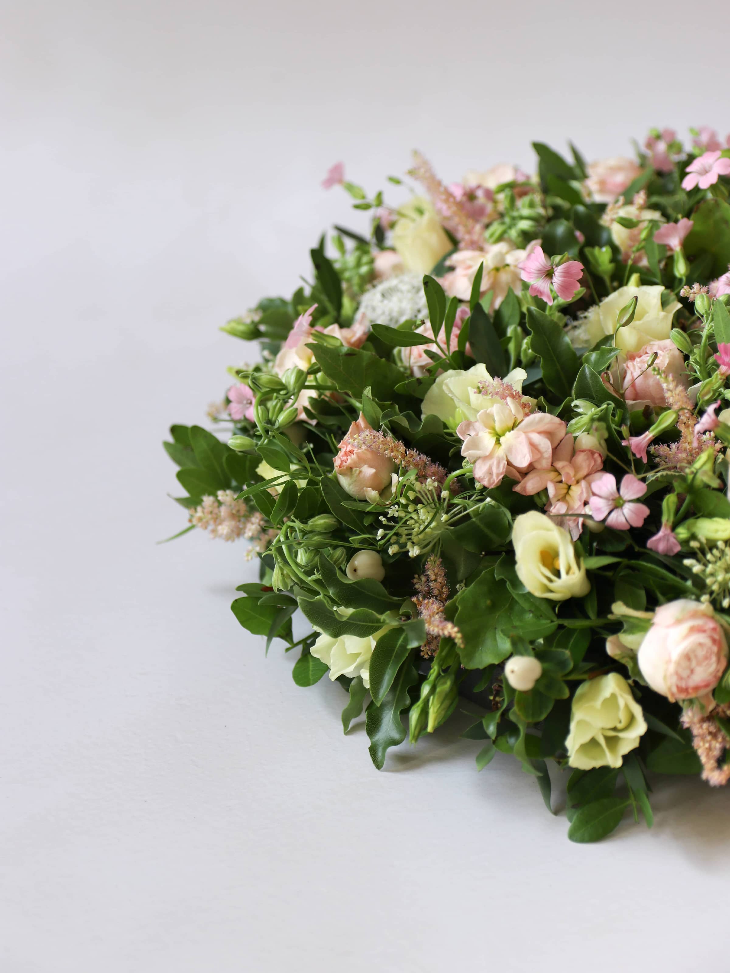 Close up of a round funeral posy with white and pastel flowers on a white background