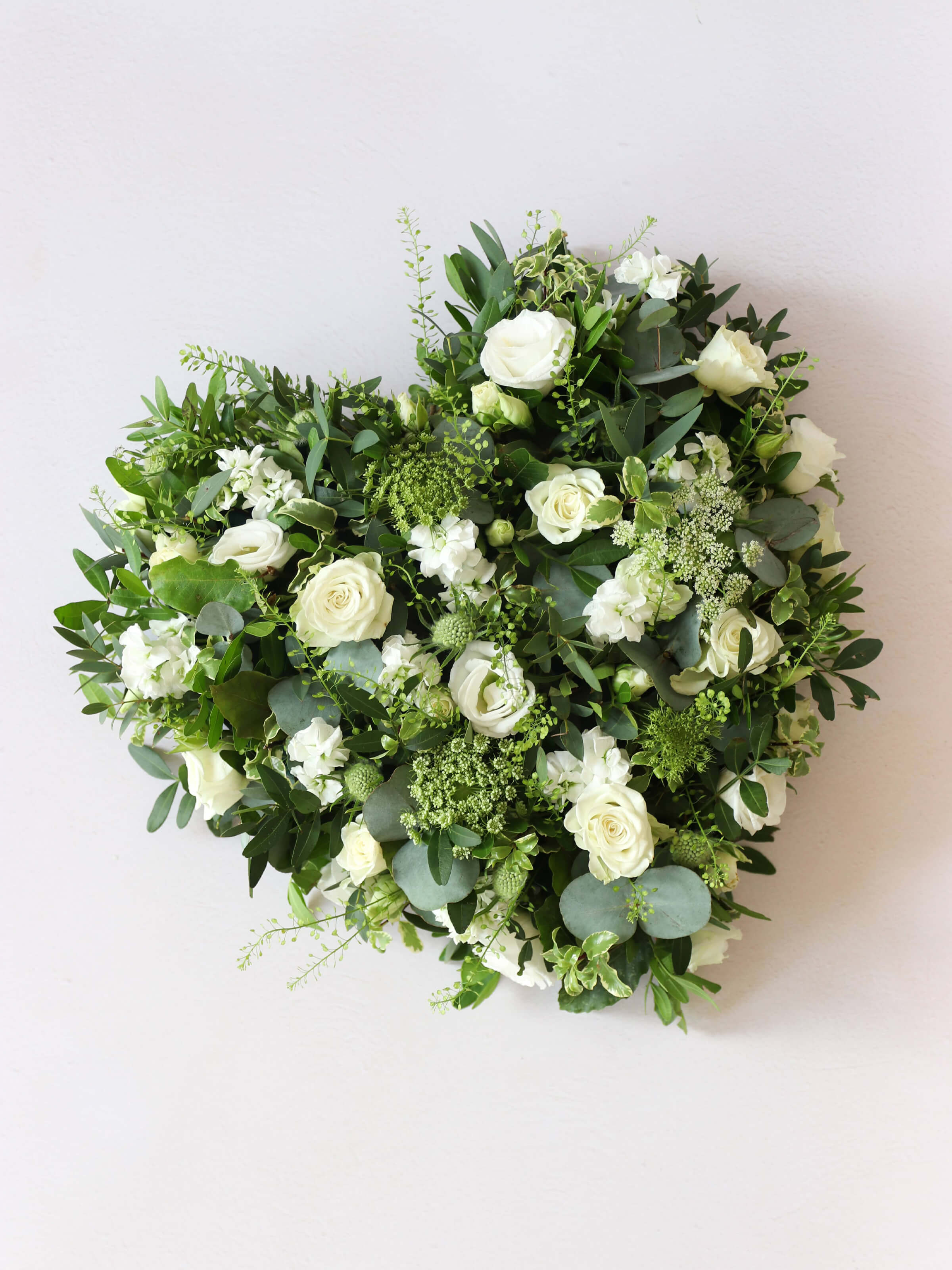 Heart shaped funeral posy with white and green flowers on a white background