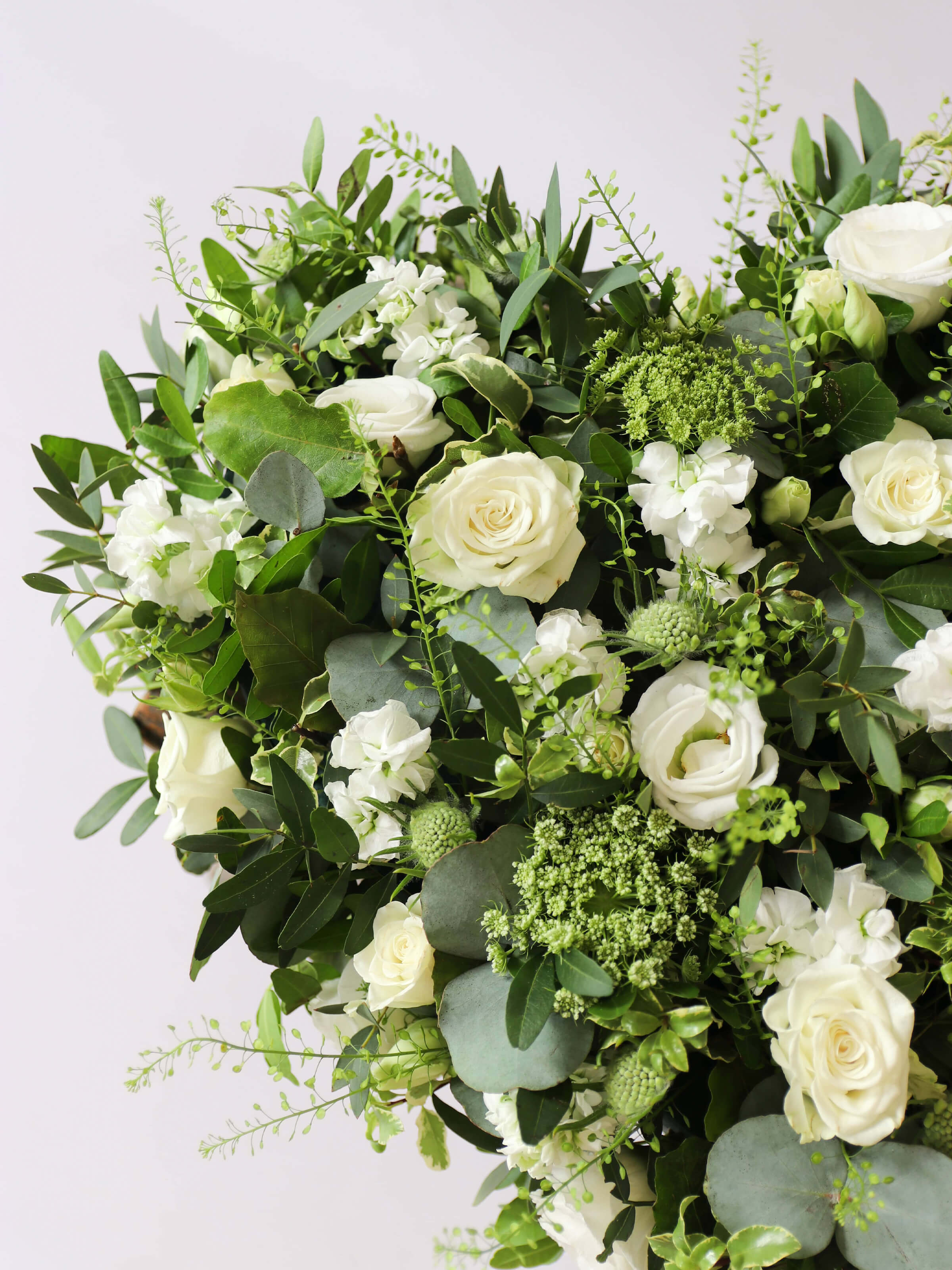 Close up of a Heart shaped funeral posy with white and green flowers on a white background