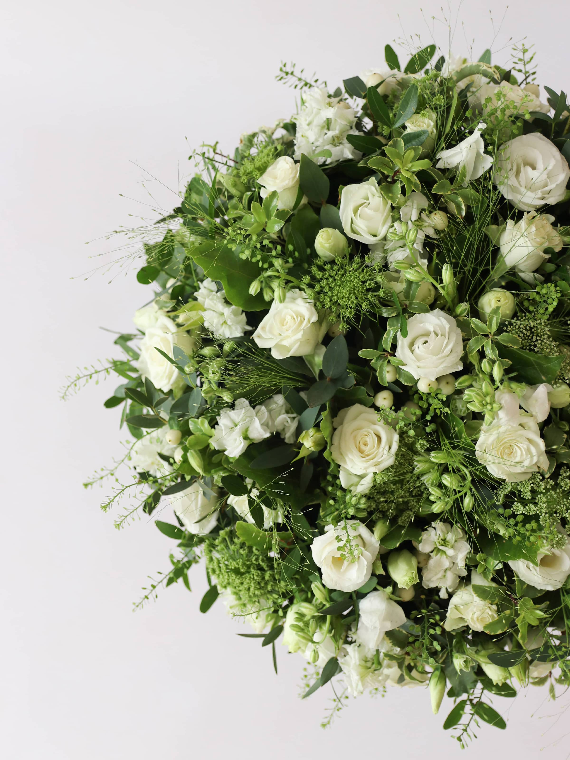 Close up of a round funeral posy with white and green flowers on a white background