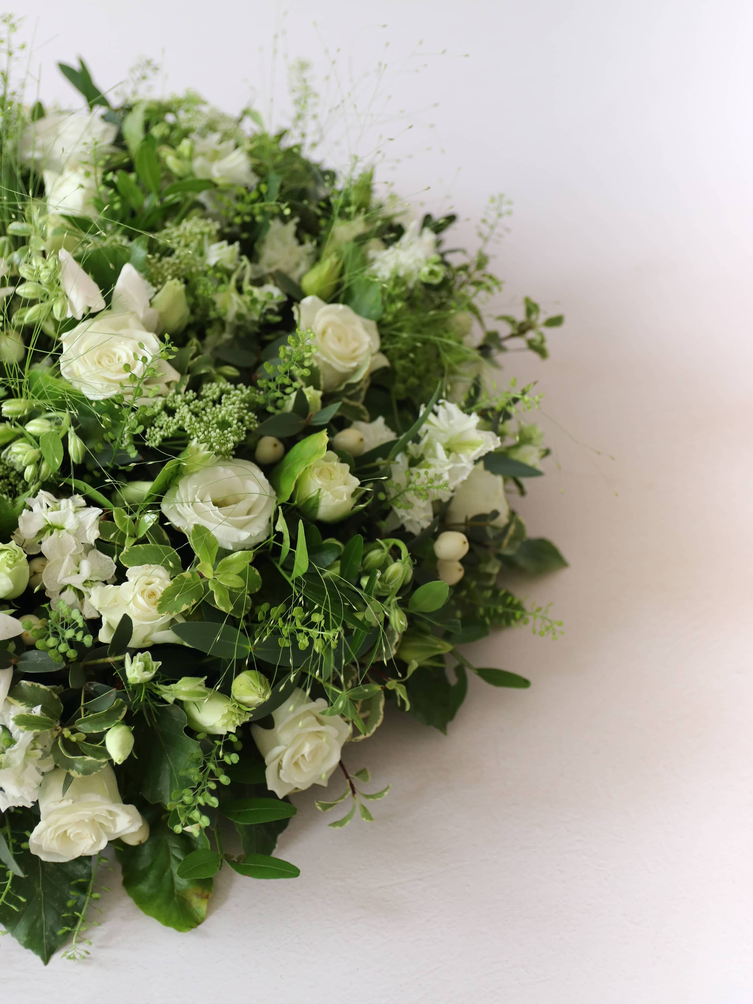 Close up of a round funeral posy with white and green flowers on a white background