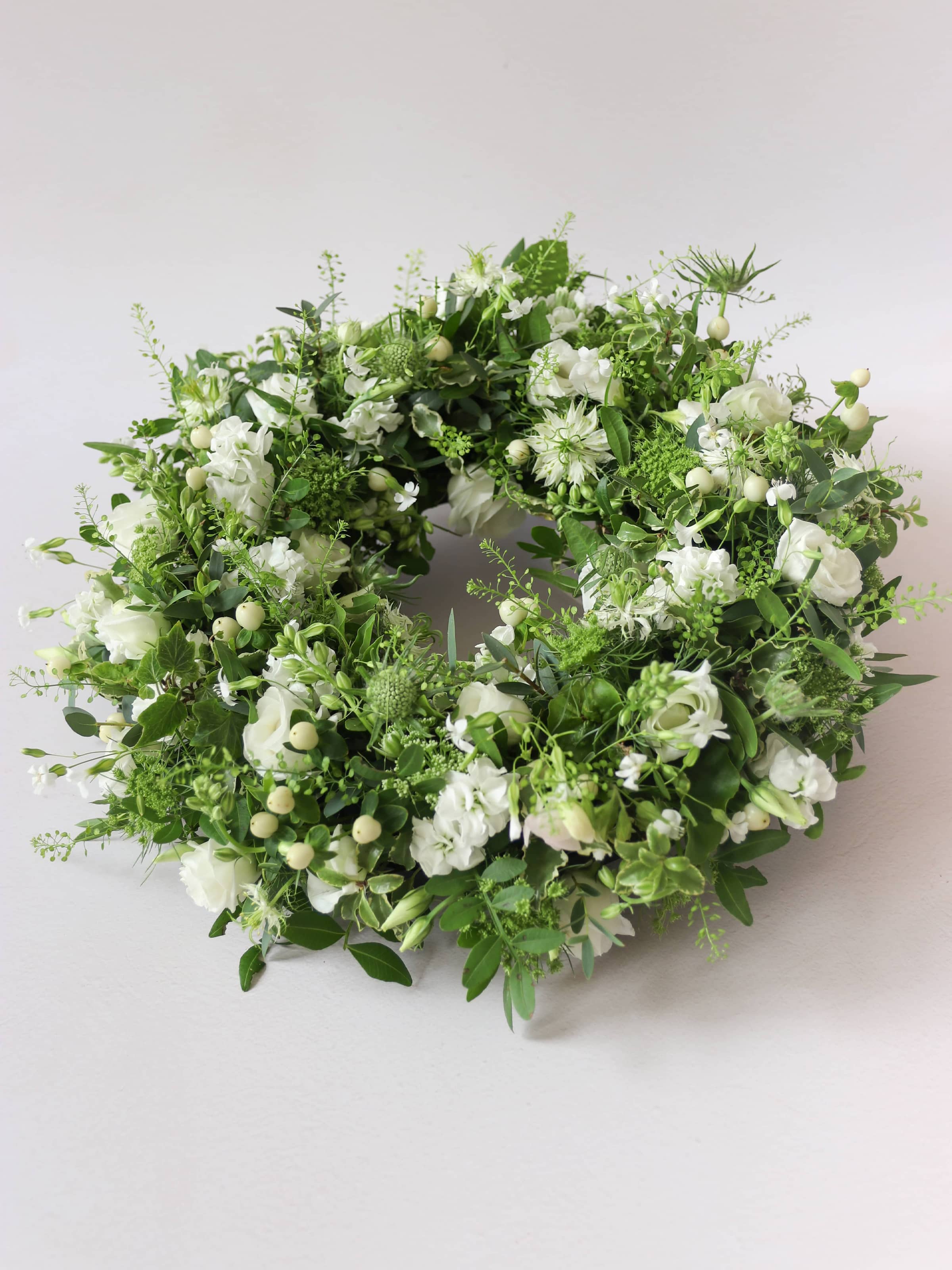 Funeral wreath with white and green flowers against a white background
