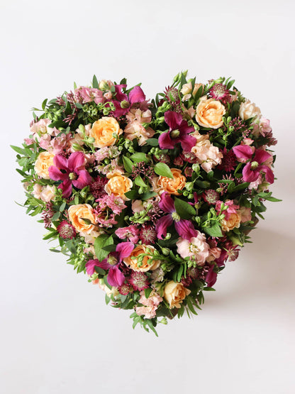 Heart-shaped funeral posy with bright pink and peach flowers on a white background