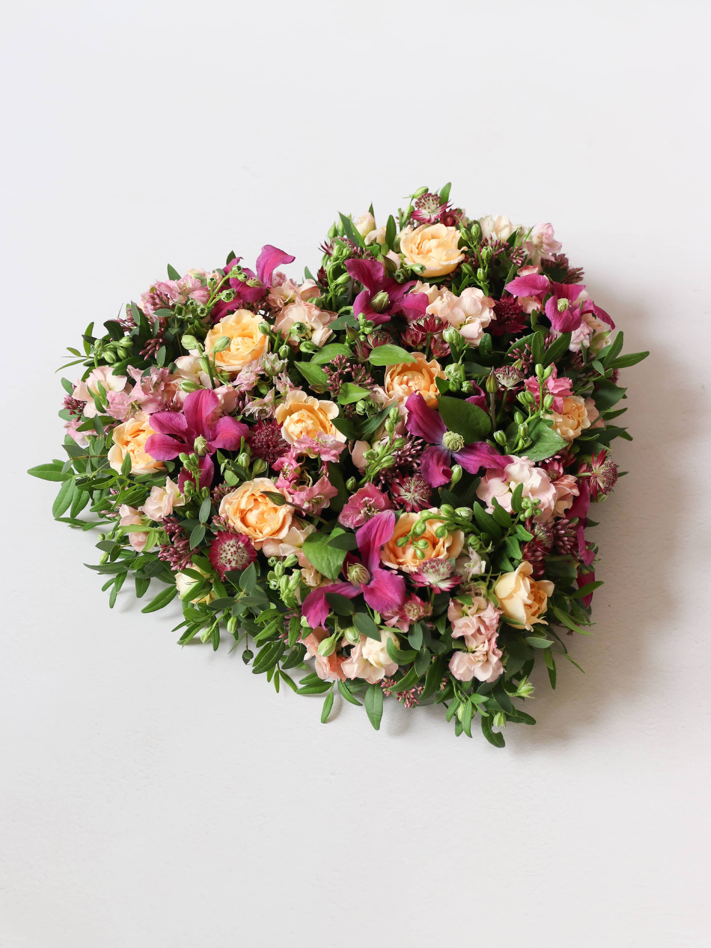 Top down, angled photo of a heart-shaped posy with bright pink and peach flowers on a white background