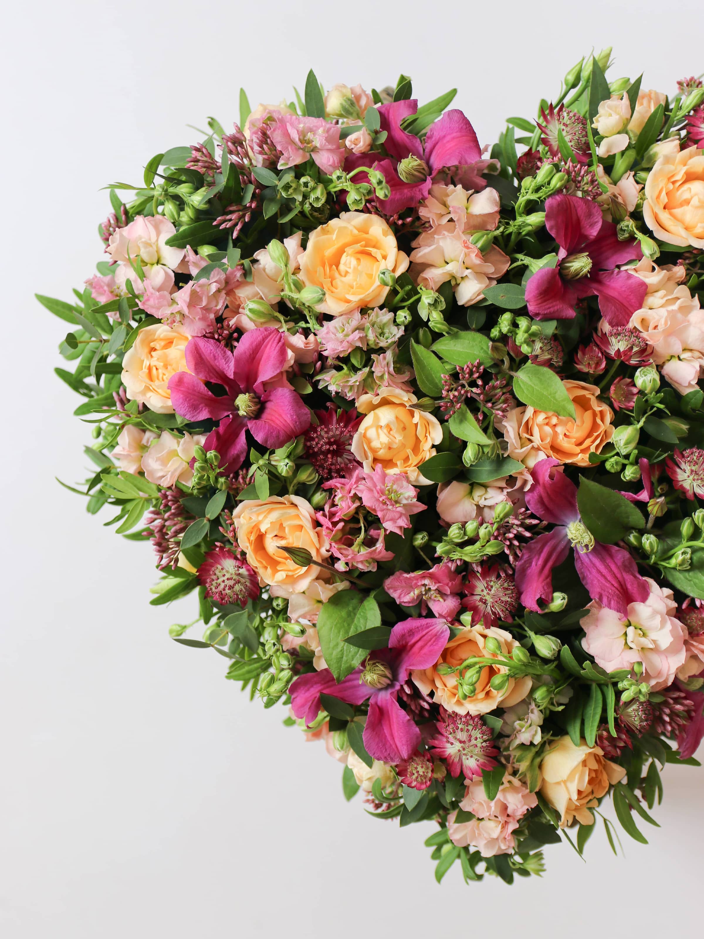 Close up, off canvas photo of a heart-shaped funeral posy with bright pink and peach flowers on a white background
