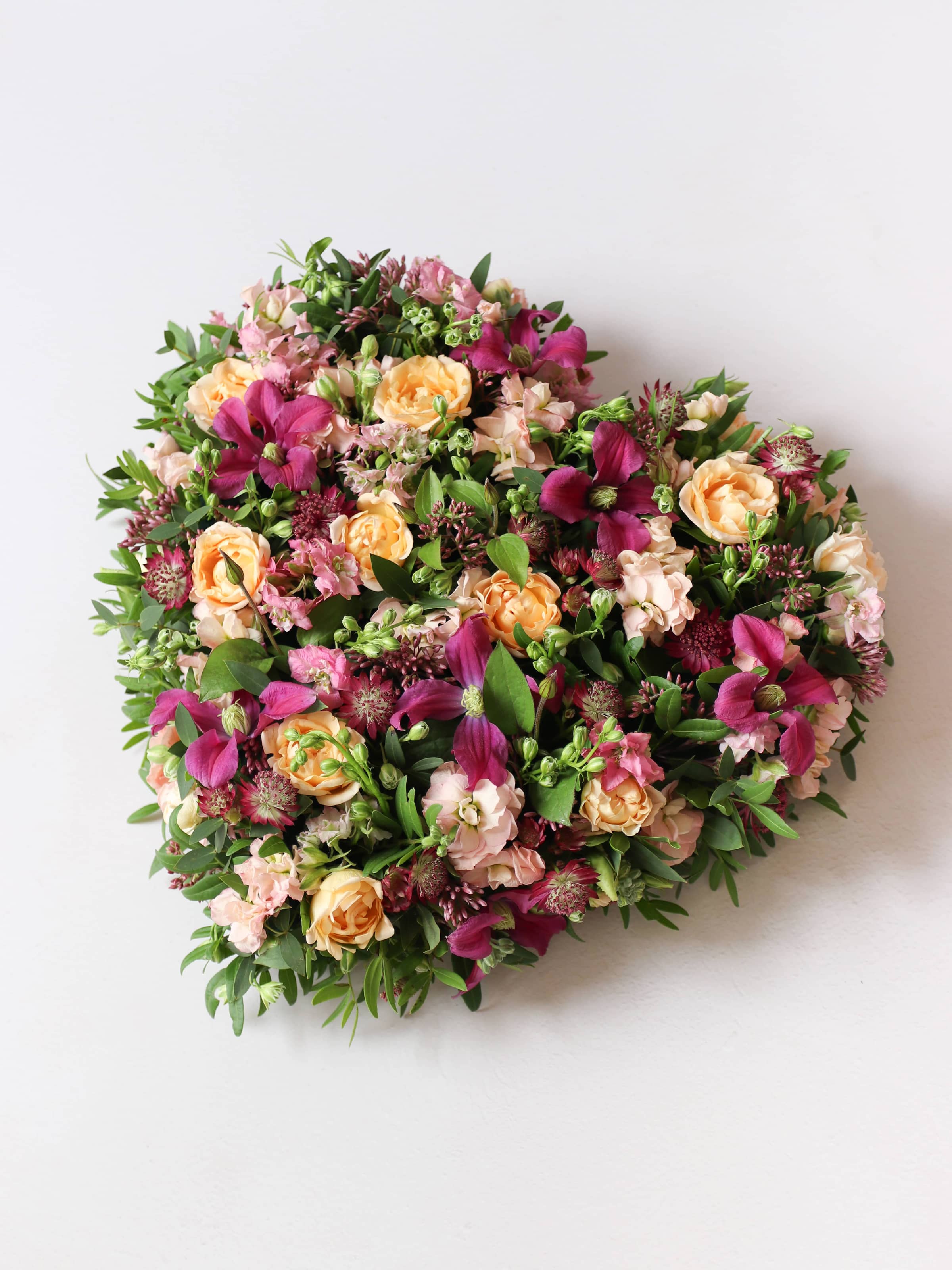 Top down view of a heart-shaped funeral posy with bright pink and peach flowers on a white background