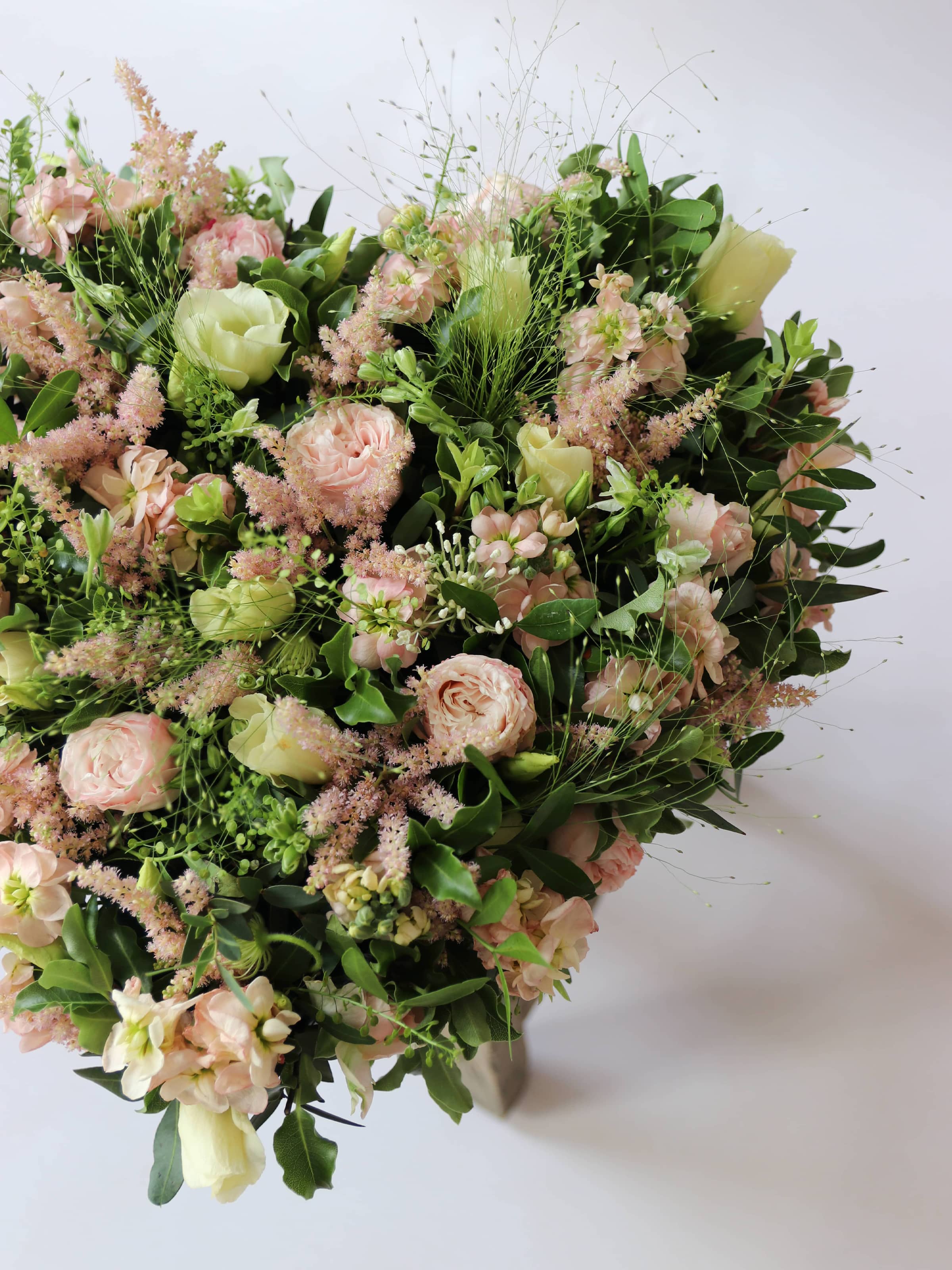 Heart shaped funeral posy with pink and green colours on a white background sitting on a wooden stool