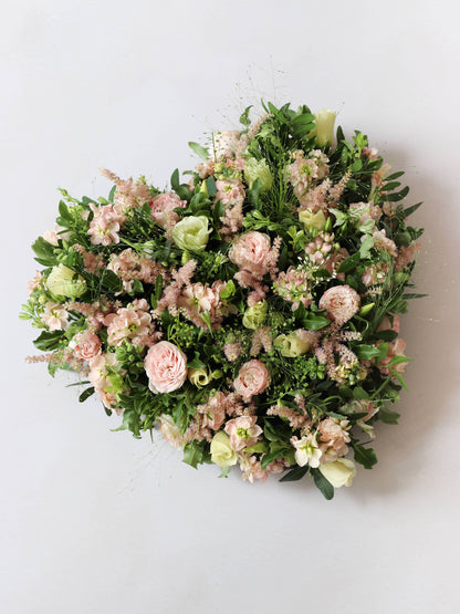 Heart shaped funeral posy with pink and green colours on a white background
