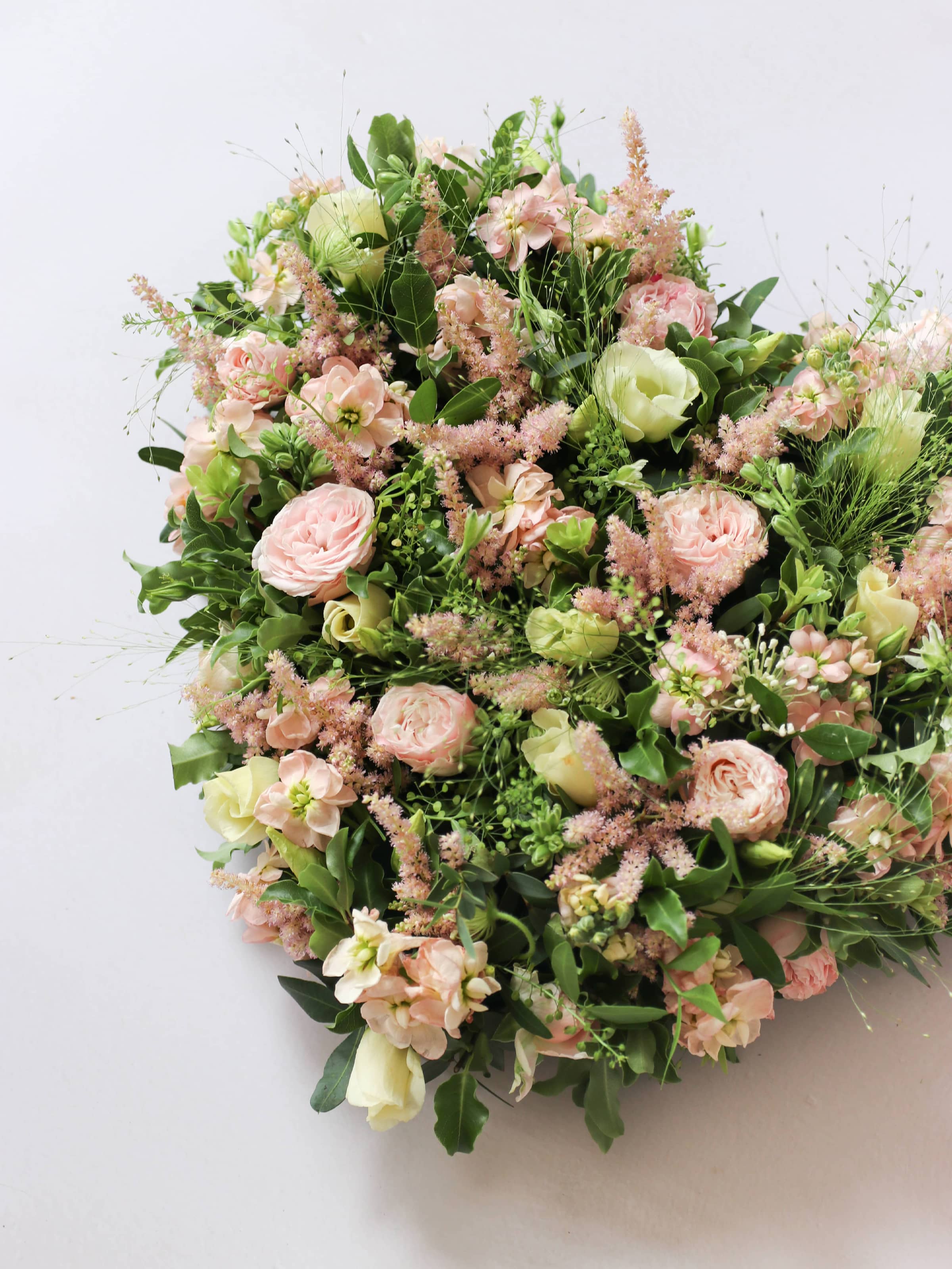 Heart shaped funeral posy with pink and green colours on a white background