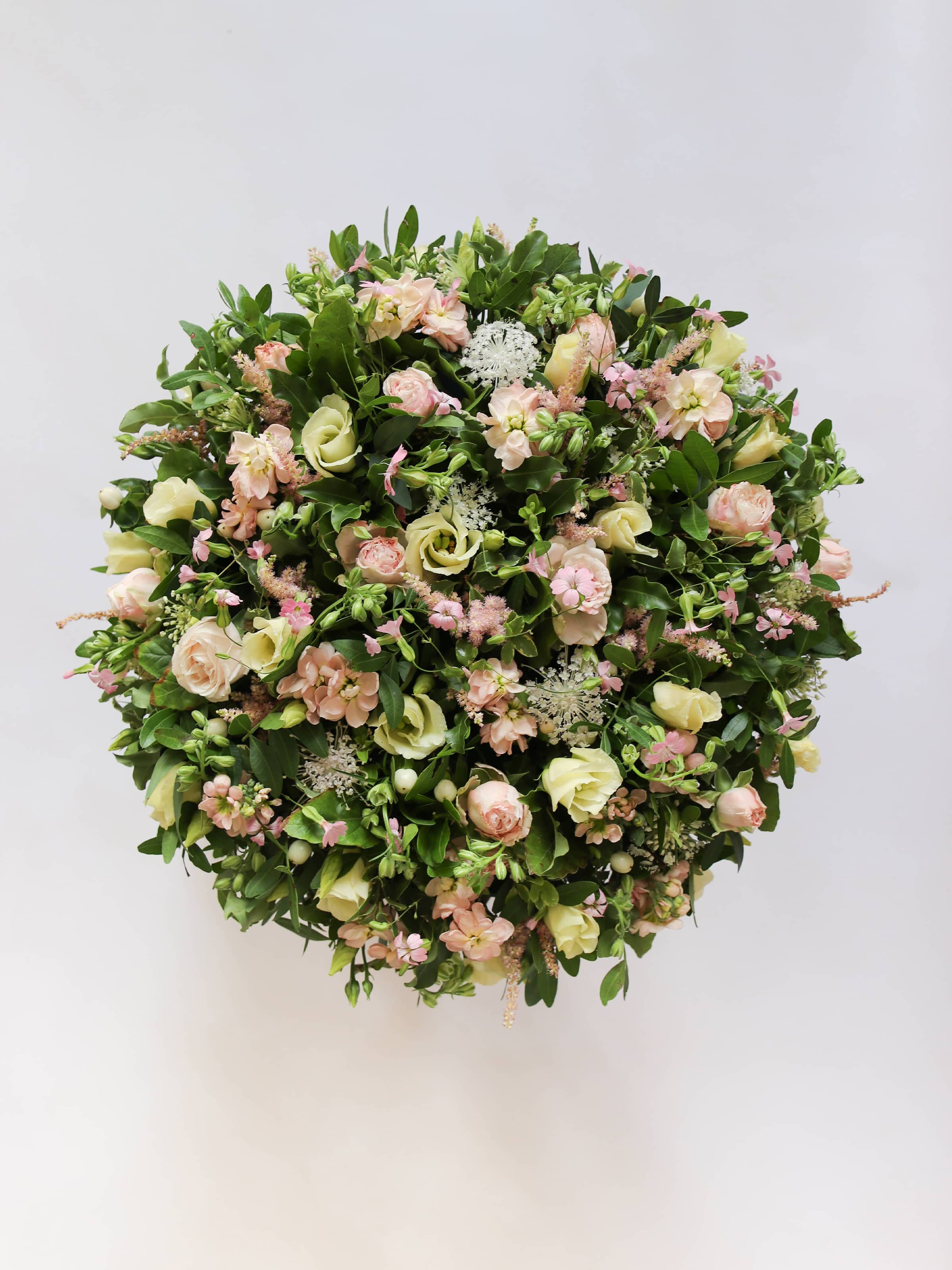 Round funeral posy with white and pastel flowers on a white background