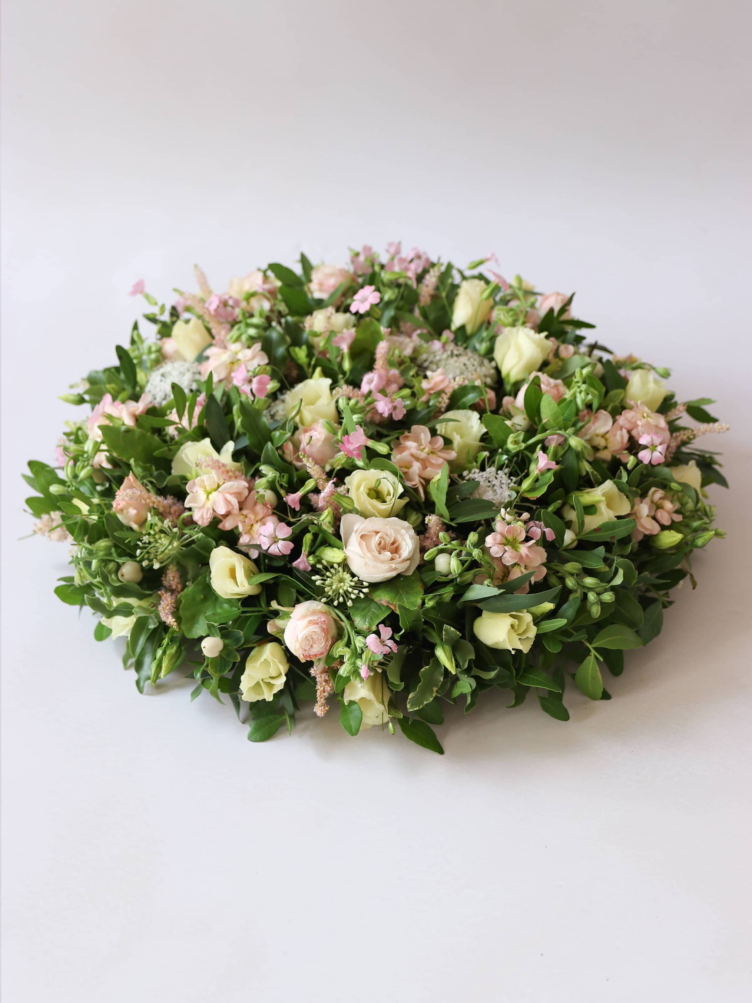 Round funeral posy with white and pastel flowers on a white background
