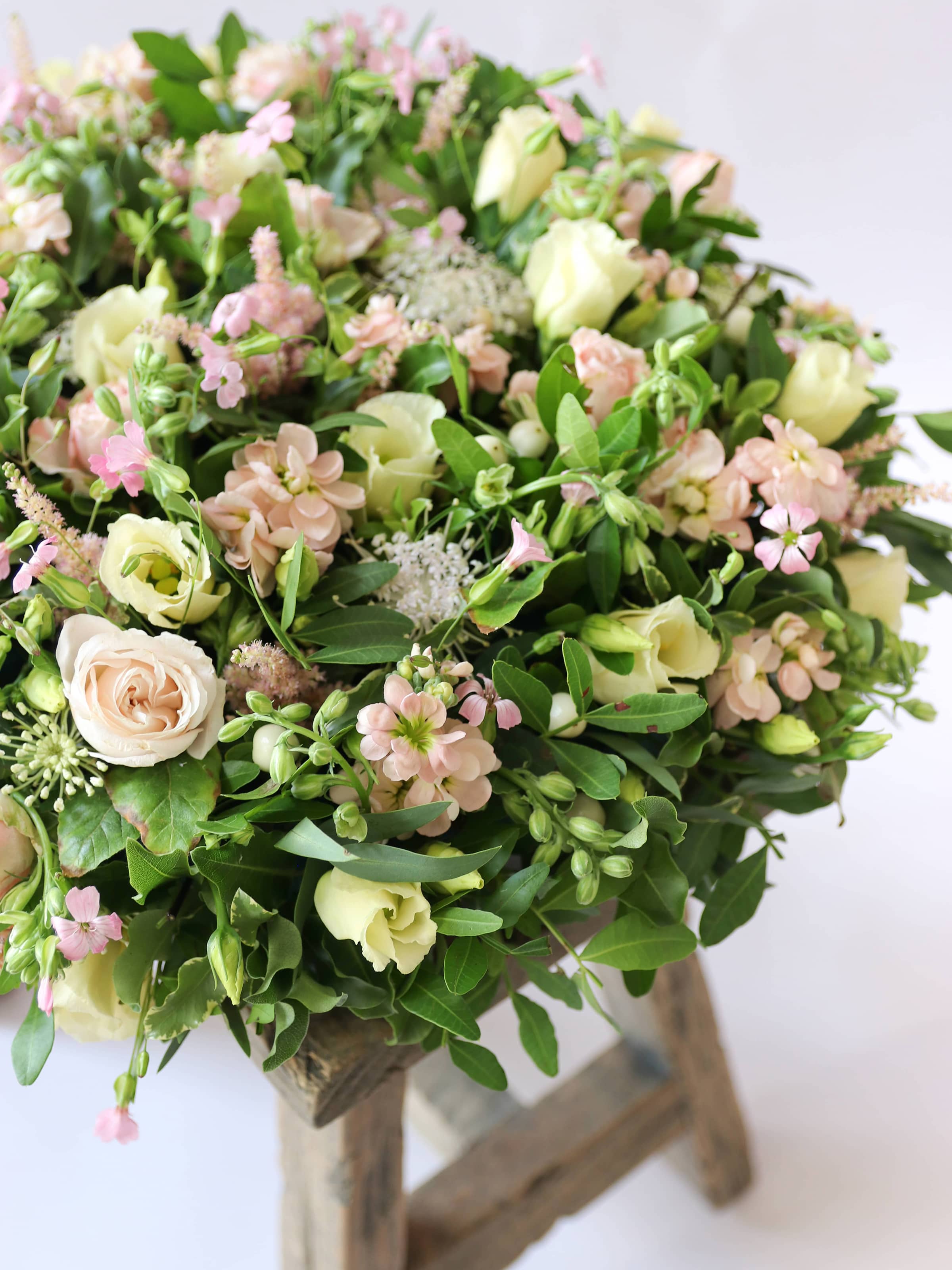 Close up of a round funeral posy with white and pastel flowers on a white background sitting on a wooden stool