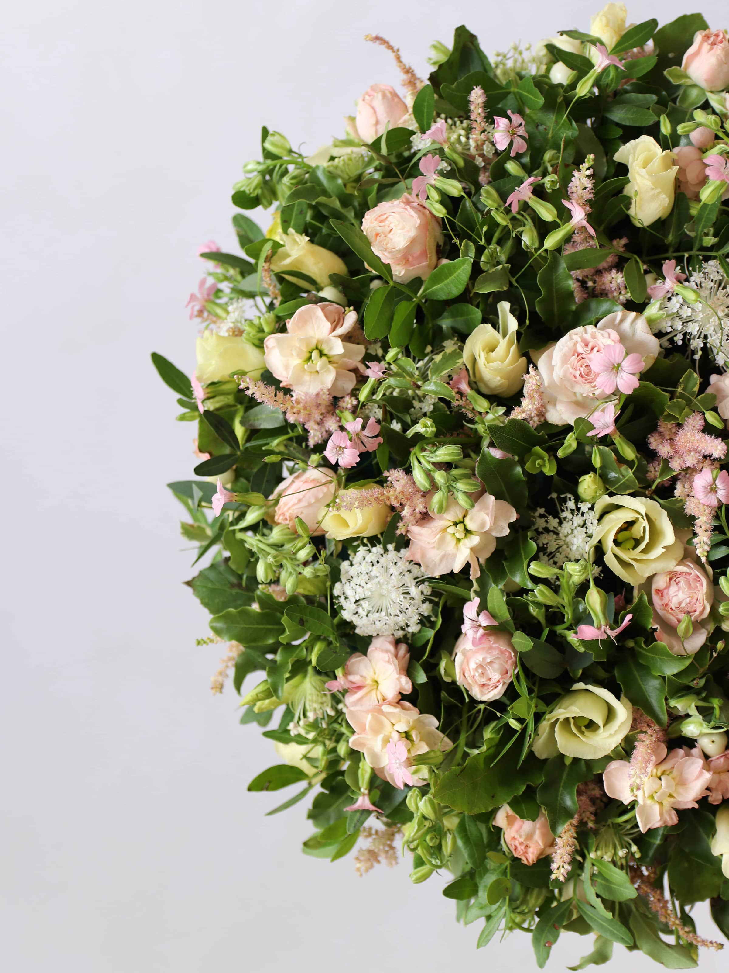 Close up of a round funeral posy with white and pastel flowers on a white background