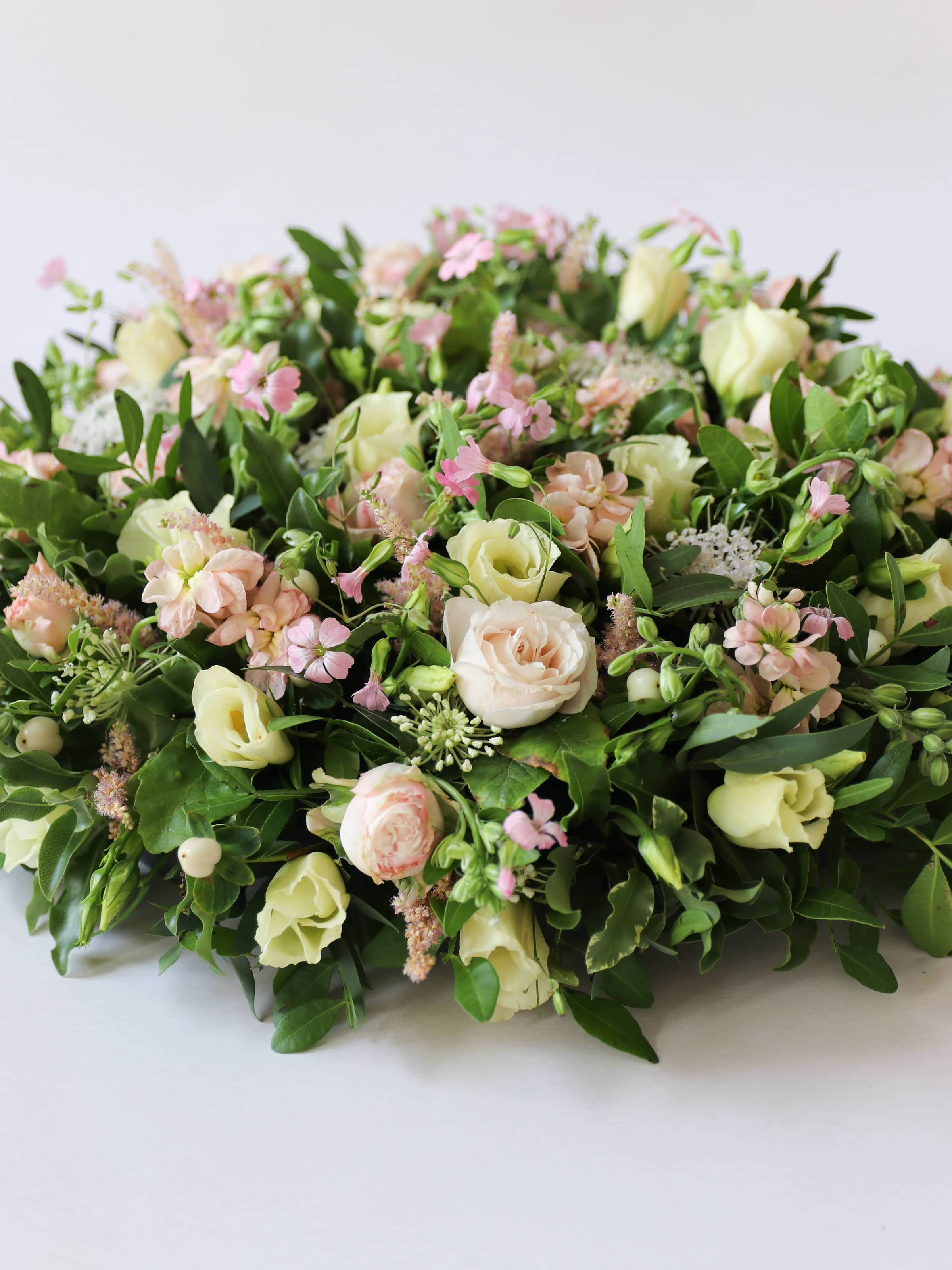 Close up of a round funeral posy with white and pastel flowers on a white background