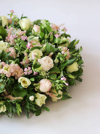 Close up of a round funeral posy with white and pastel flowers on a white background