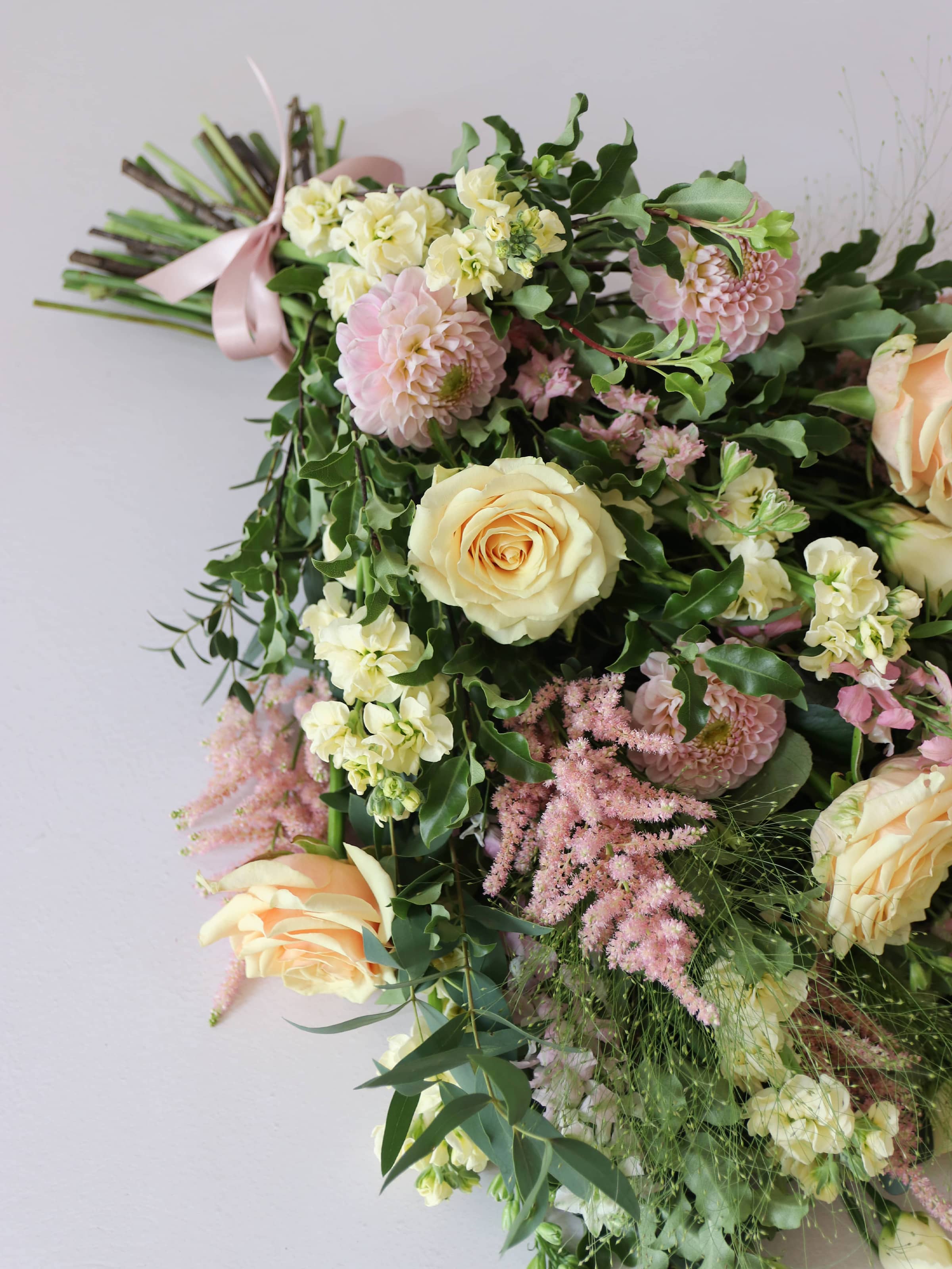 A top down view of a pastel tied funeral sheaf containing pastel pink, peach and yellow flowers, tied with a satin pink ribbon.