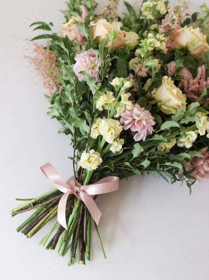A detailed view of a satin pink ribbon on a  pastel tied funeral sheaf containing pastel pink, peach and yellow flowers.