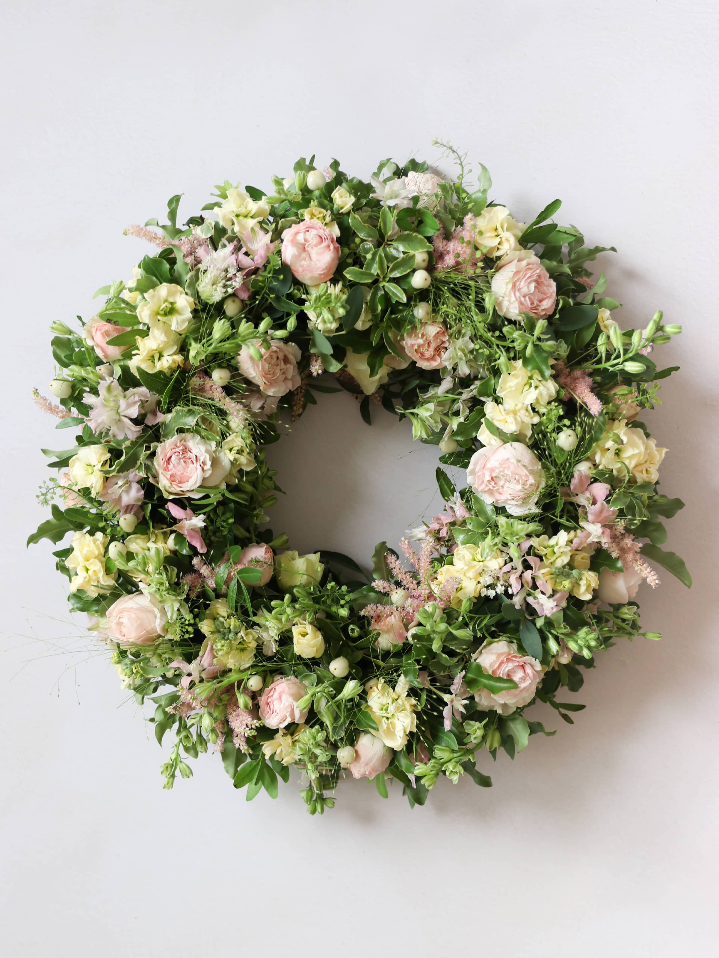 Top down view of a funeral wreath with pastel and green flowers against white background