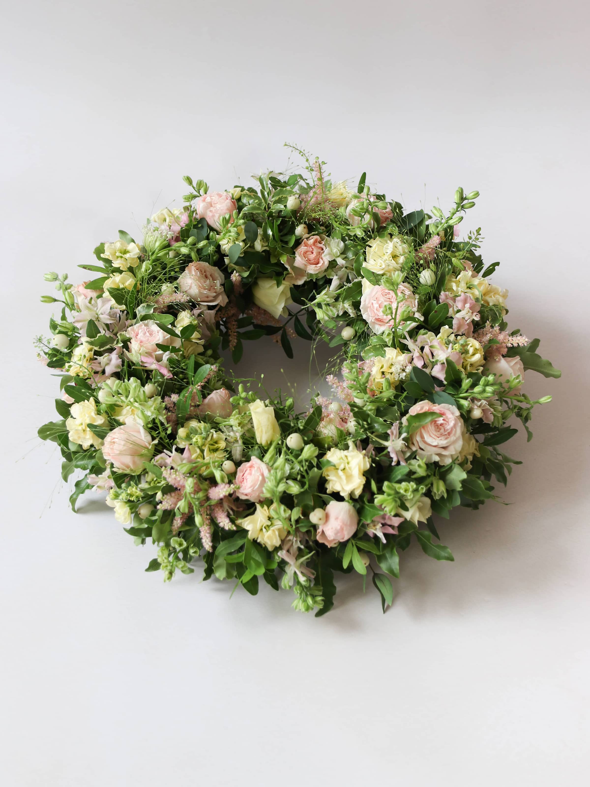 Top down view of a funeral wreath with pastel and green flowers against white background