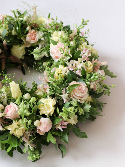 Close up of a funeral wreath with pastel and green flowers against white background