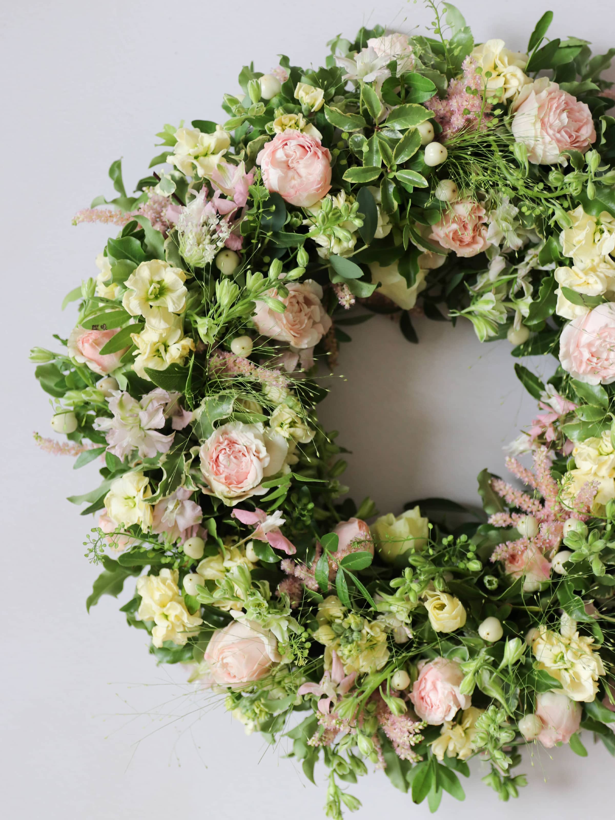 Top down view of close up image of a funeral wreath with pastel and green flowers against white background