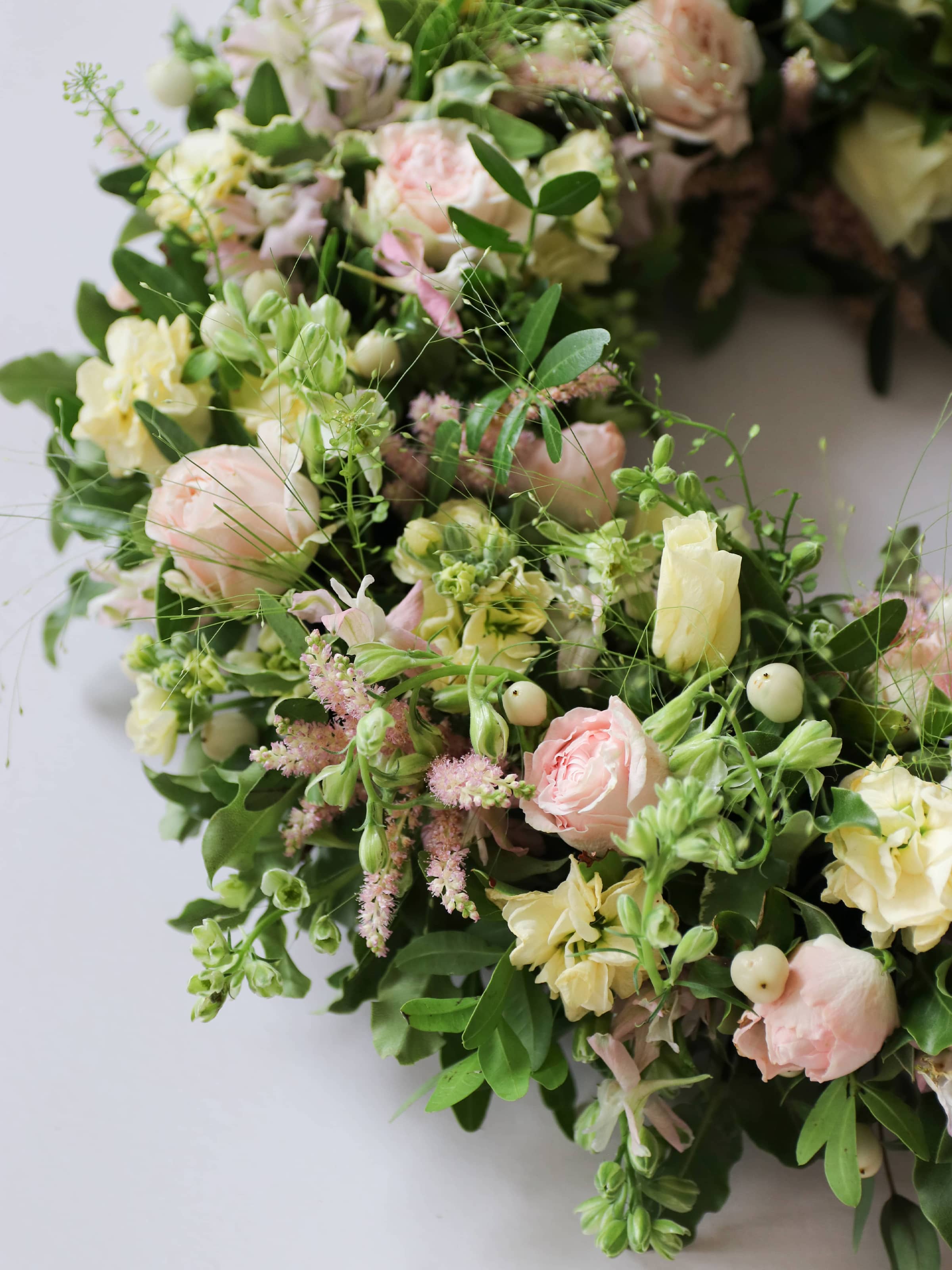 Close up view of a funeral wreath with pastel and green flowers against white background