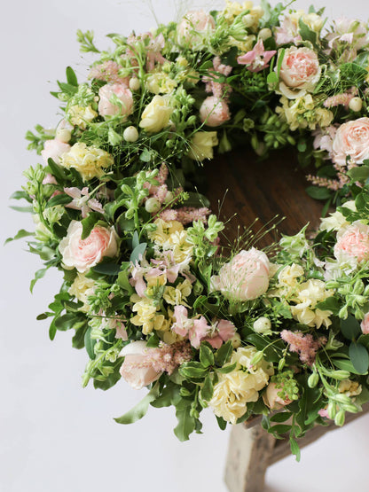 Top down view of a funeral wreath with pastel and green flowers against white background on a wooden stool