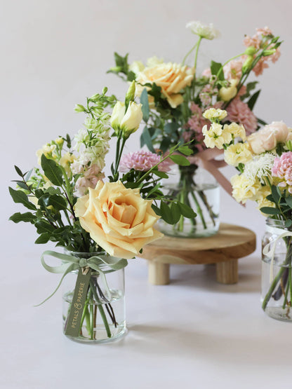 A close up of jam jars with pastel coloured flowers sitting on a wooden stool against a light background