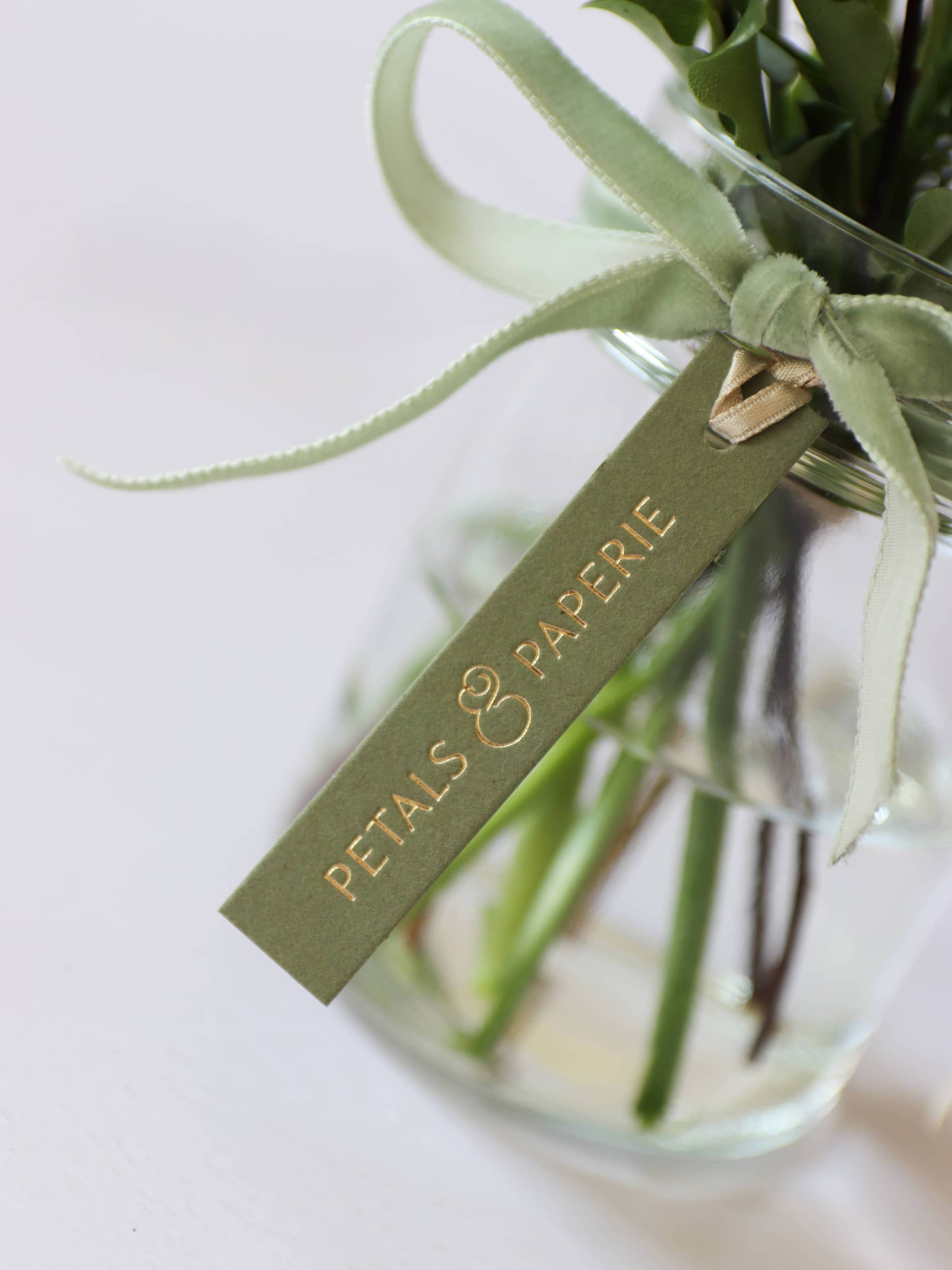 A close up of a green and gold foiled Petals & Paperie brand tag on a bouquet of flowers