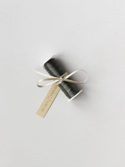 A spool of silver reel wire for Christmas wreath making, tied with a cream satin ribbon and Petals & Paperie gift tag on a neutral background.