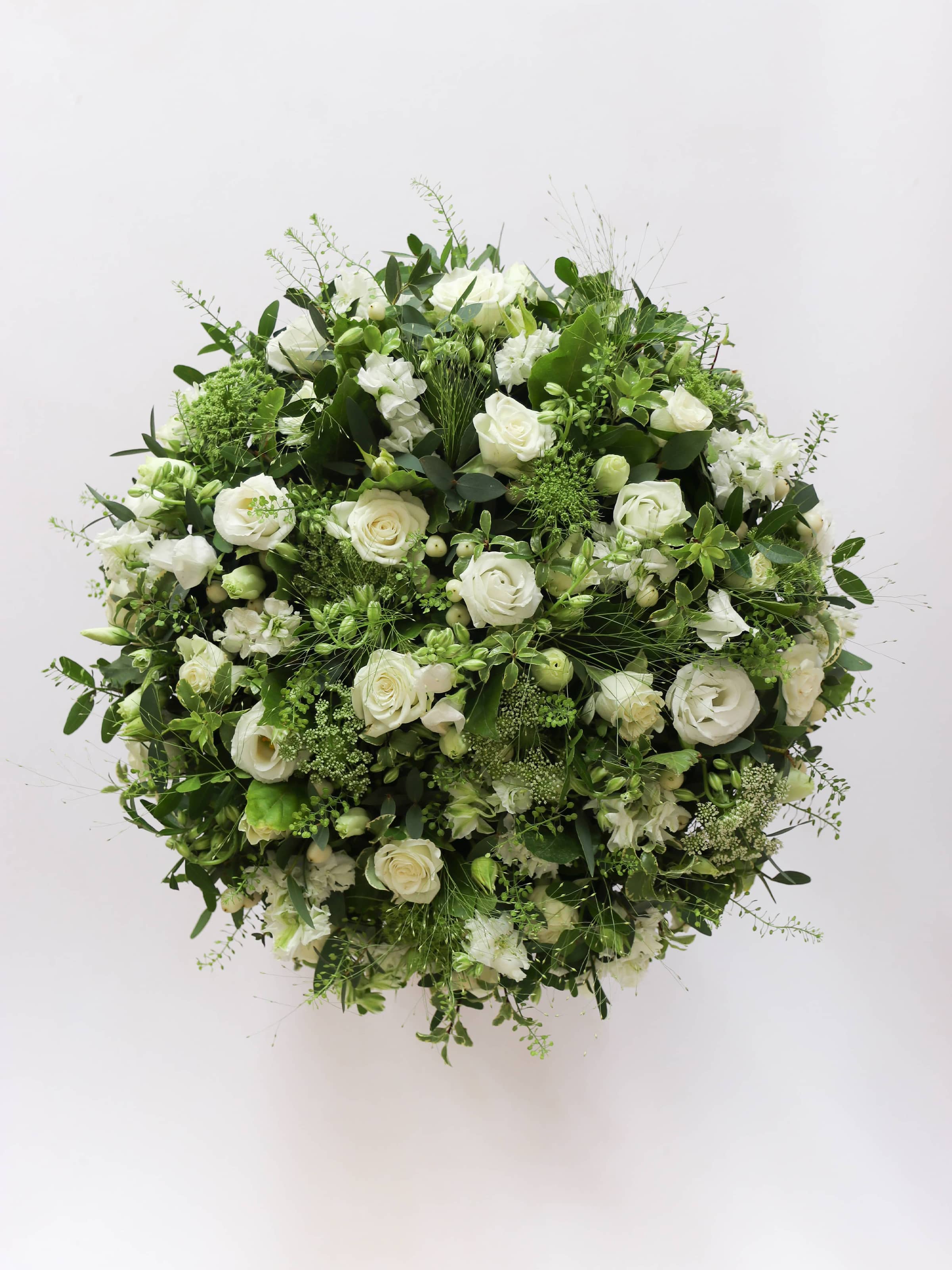 Round funeral posy with white and green flowers on a white background