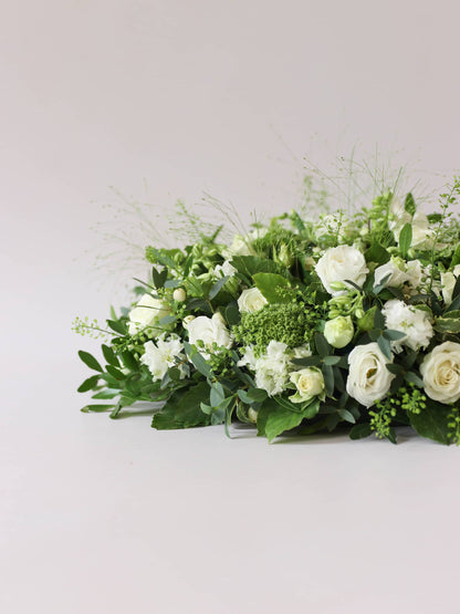 Side view of a round funeral posy with white and green flowers on a white background