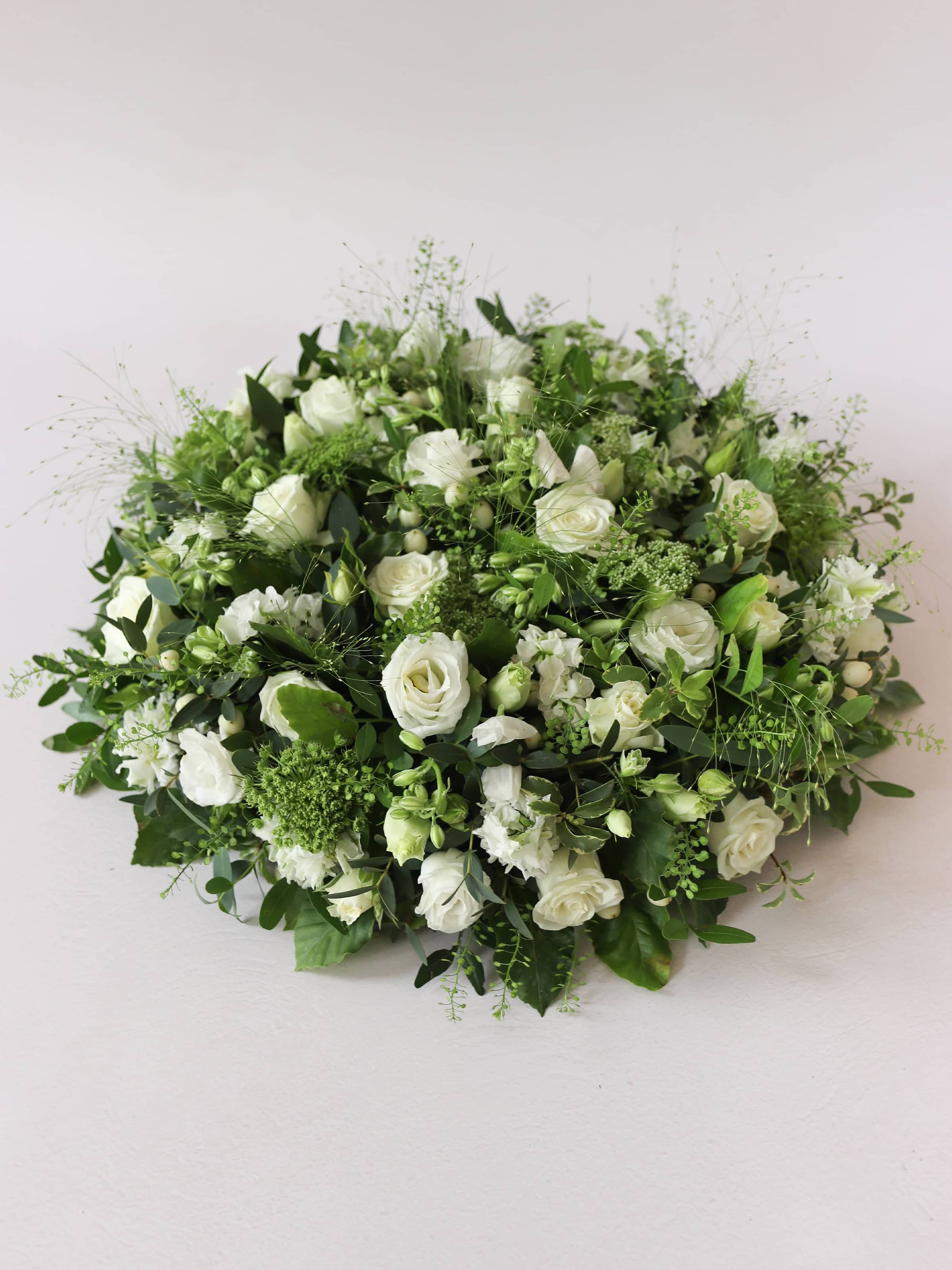 Round funeral posy with white and green flowers on a white background