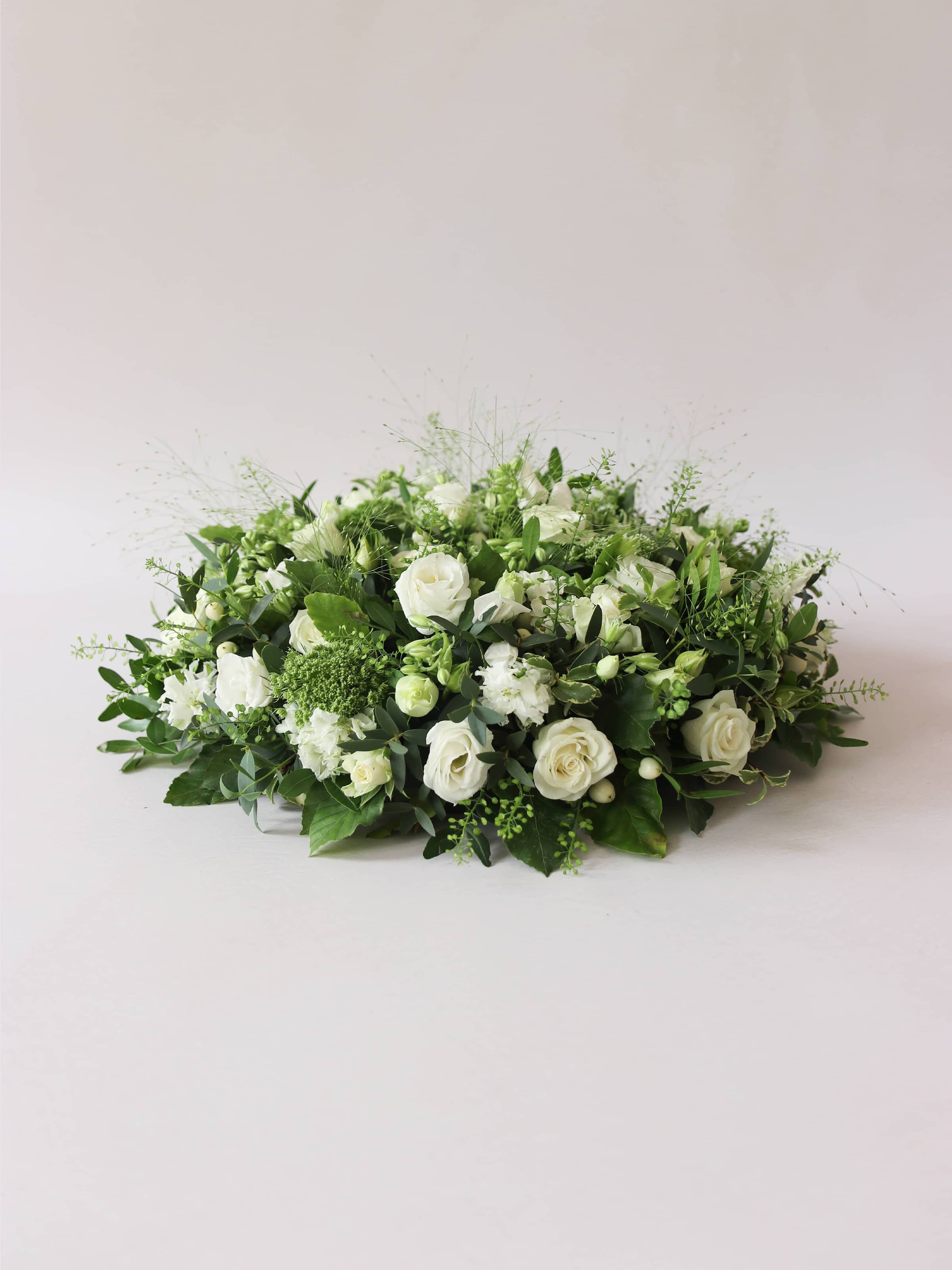 Round funeral posy with white and green flowers on a white background