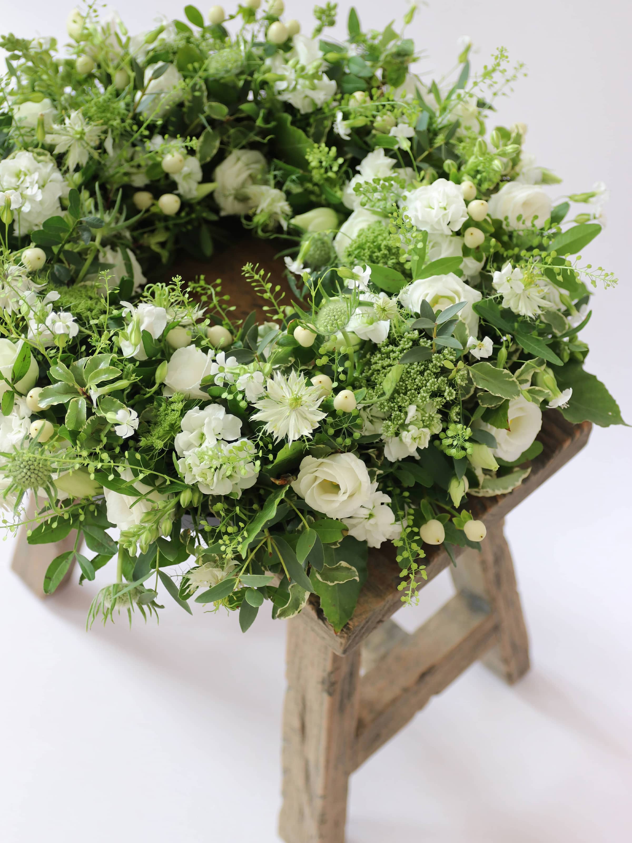 Funeral wreath with white and green flowers on a wooden stool against a white background