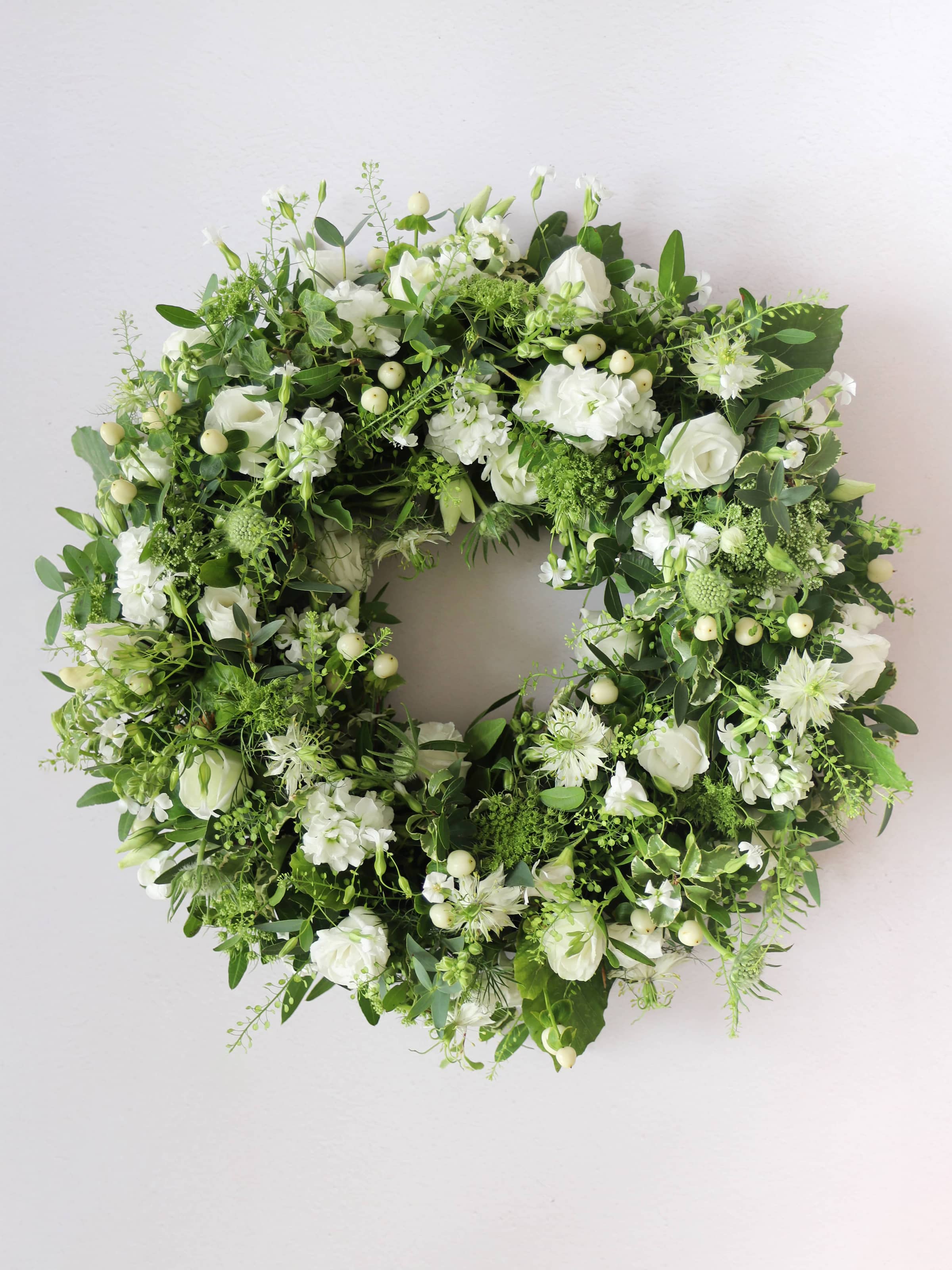Funeral wreath with white and green flowers against a white background
