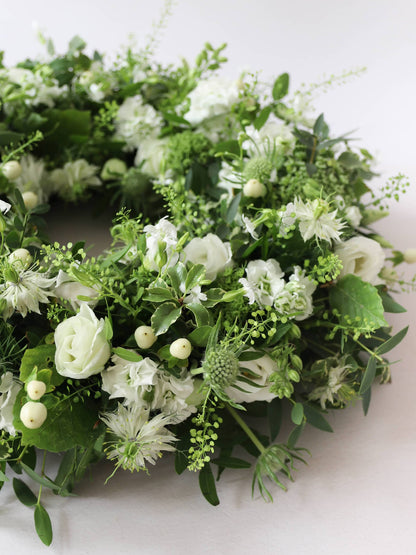 Close up of a funeral wreath with white and green flowers against a white background