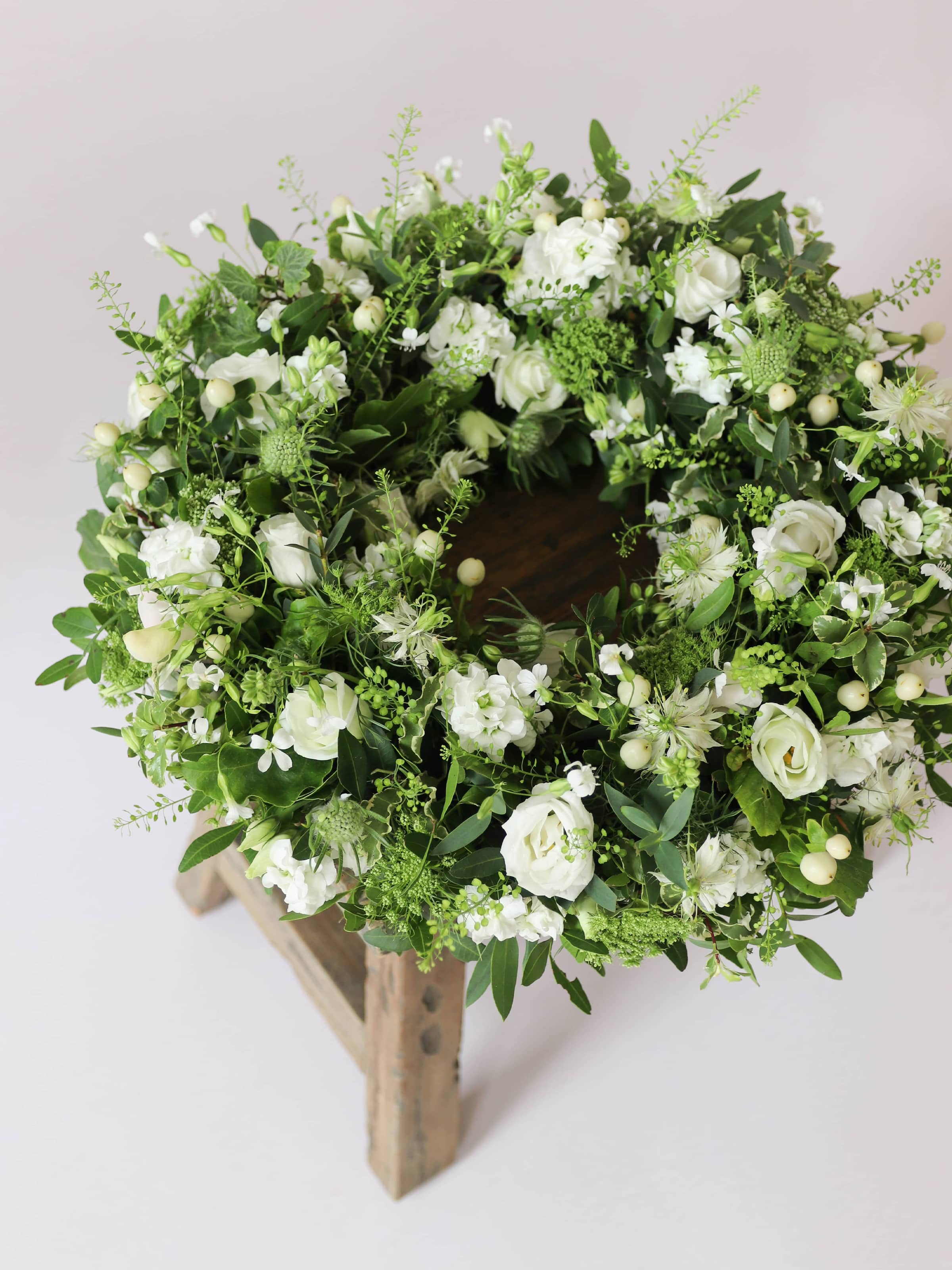 Funeral wreath with white and green flowers on a wooden stool against a white background