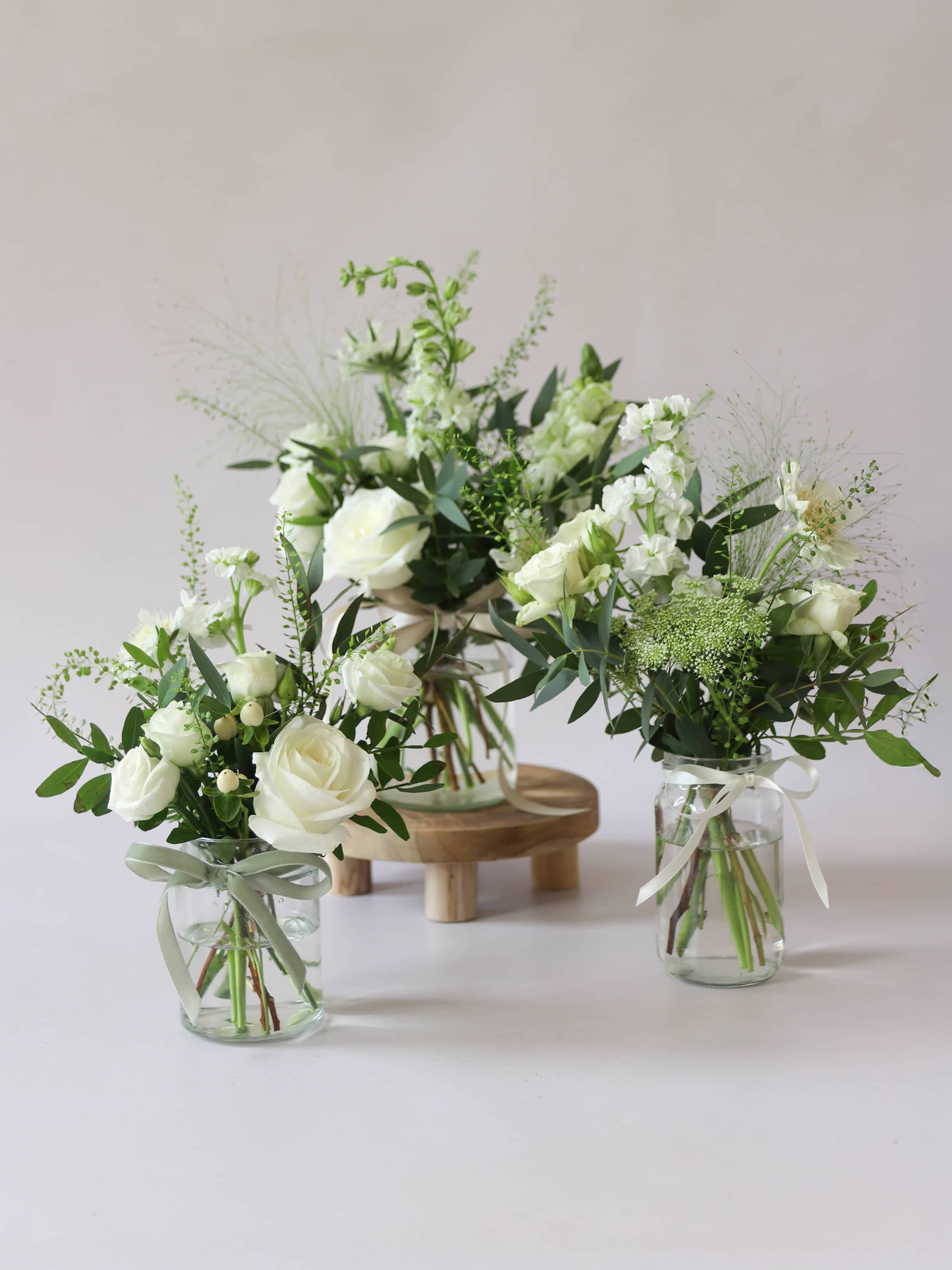 Three glass jars with white and green flowers on a light background
